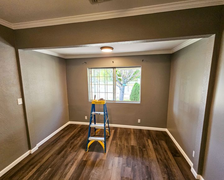 A room in the process of being renovated, featuring freshly painted walls, a ladder for painting, and wooden flooring.