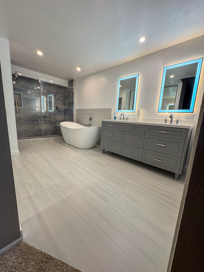A beautifully remodeled bathroom with gray cabinetry, white fixtures, and modern LED-lit mirrors, showcasing elegance and functionality.