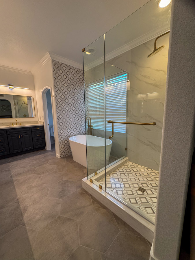 A refined bathroom design with gold fixtures, hexagonal floor tiles, and a glass-enclosed shower area, highlighting luxury and sophistication.